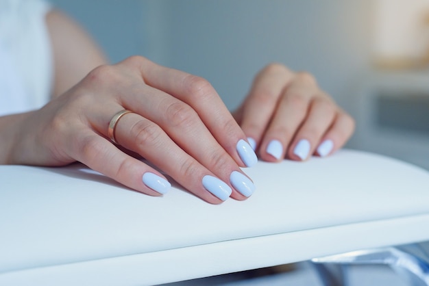 Belles mains féminines avec une manucure bleue douce sur un stand au salon de beauté