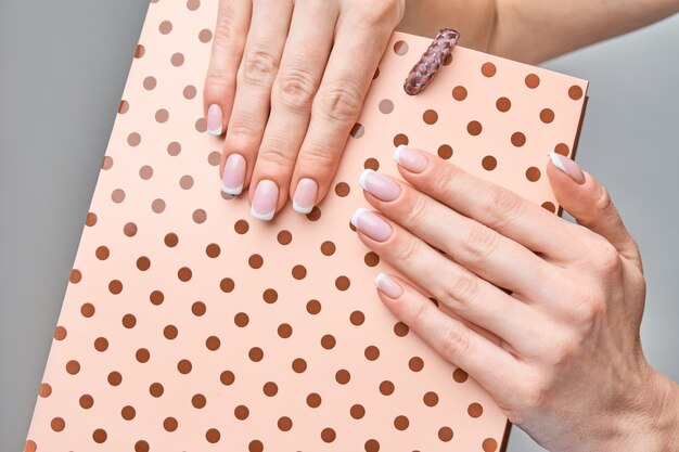 Belles mains féminines avec manucure française sur fond gris clair.