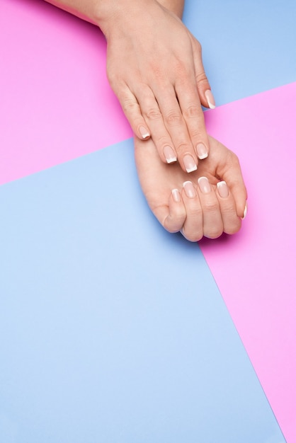 Belles mains féminines avec manucure française sur la surface du papier coloré