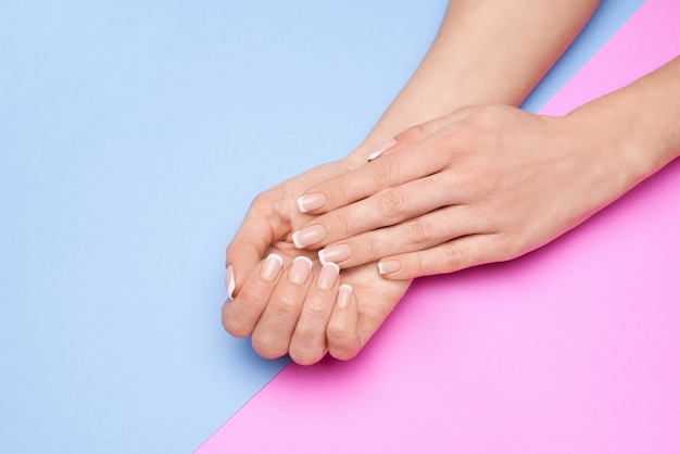 Belles mains féminines avec manucure française sur la surface du papier coloré