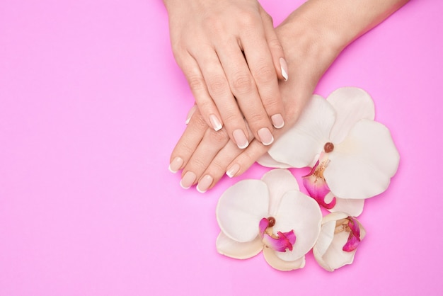 Belles mains féminines avec manucure française sur surface rose.