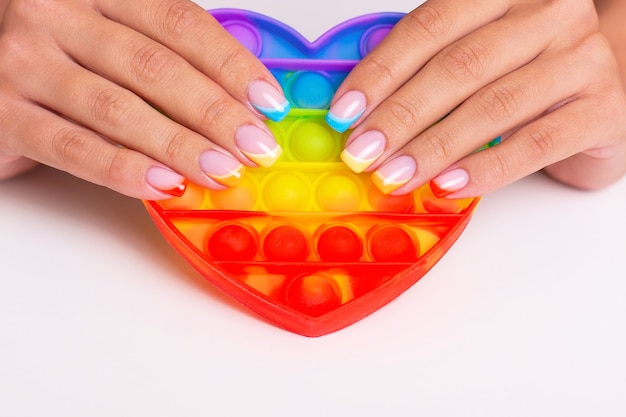 Belles mains féminines avec des ongles de manucure colorés tenant un jouet pop it