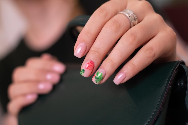 Belles mains féminines avec des ongles de manucure créatifs, un vernis gel rose, un design de feuilles tropicales