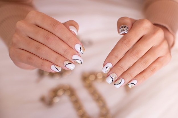 Belles mains féminines avec des ongles de manucure de luxe vernis gel blanc sur fond de chaîne dorée