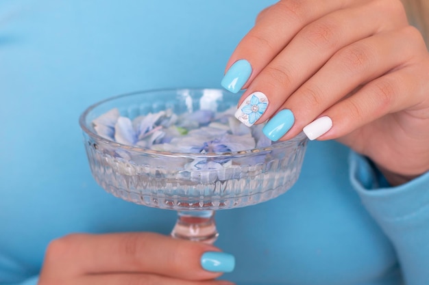 Belles mains féminines avec des ongles de manucure romantique, vernis gel bleu et blanc