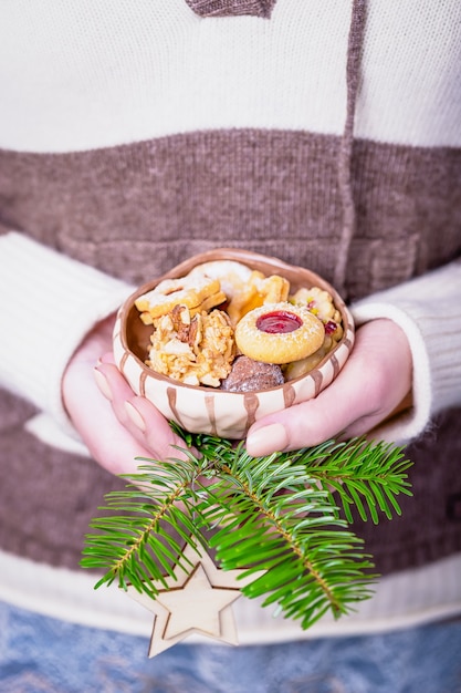Belles mains féminines tenant un bol avec des biscuits faits maison et une branche d'arbre de Noël