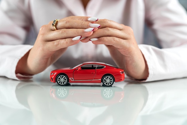 De belles mains féminines tiennent au-dessus de la voiture rouge comme protection des concepts de voiture de protection de voiture d'assurance automobile