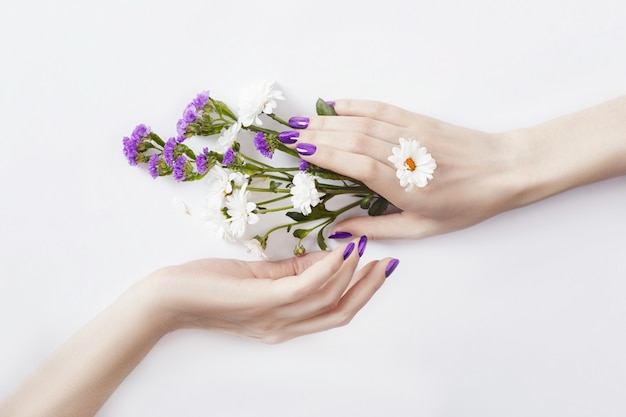 De belles mains soignées avec des fleurs sauvages sur la table, des cosmétiques anti-âge et anti-rides pour les mains. Soins et beauté de la peau, hydratation de la peau et Spa