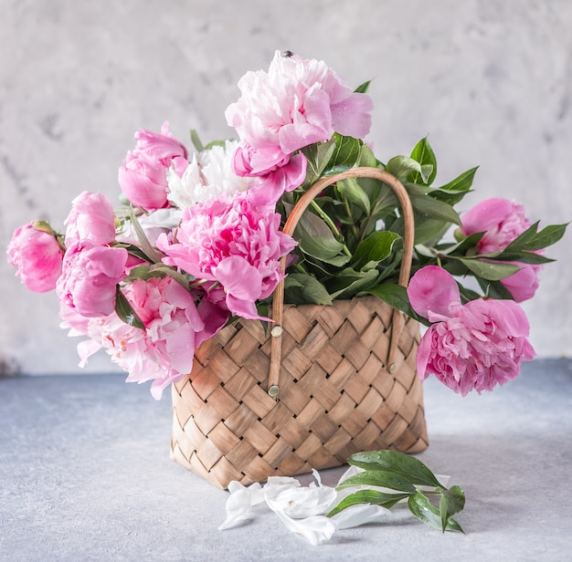 Belles pivoines dans un panier en osier sur une table en bois