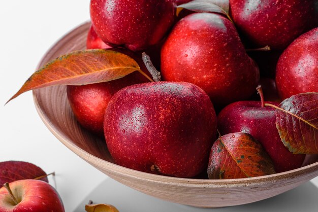 Belles pommes rouges fraîches avec des feuilles d'automne dans un vase en bois sur une table en béton clair. La saison des récoltes
