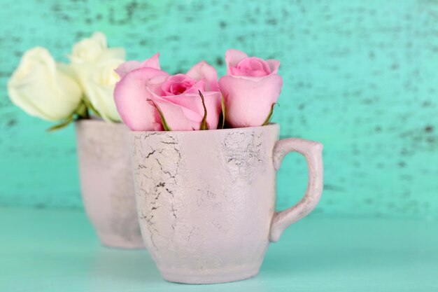 Belles roses dans des tasses sur fond bleu