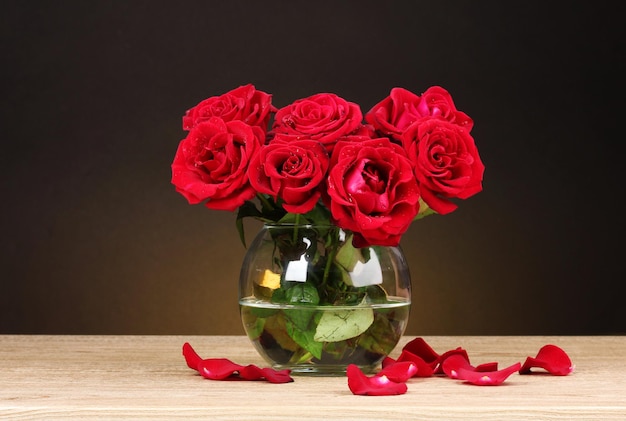 Belles roses rouges dans un vase sur une table en bois sur fond marron
