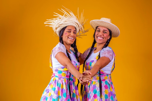 Belles soeurs jumelles portant des vêtements traditionnels pour la fête de juin dansant sur fond jaune