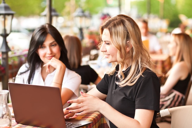 Belles travailleuses ou étudiantes utilisant un ordinateur portable au café et parlant.