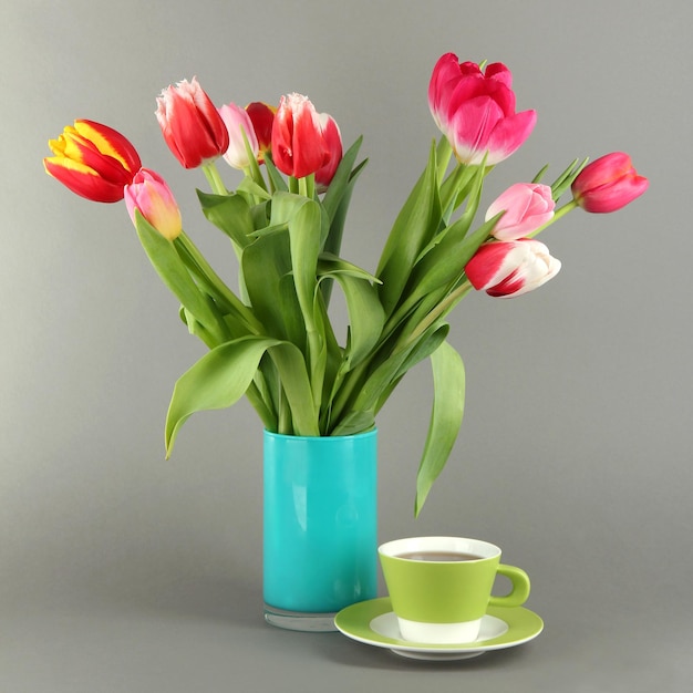 Belles tulipes dans un seau avec une tasse de thé sur fond gris