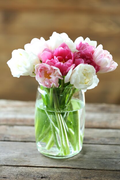 Belles tulipes dans un vase en verre sur fond de bois