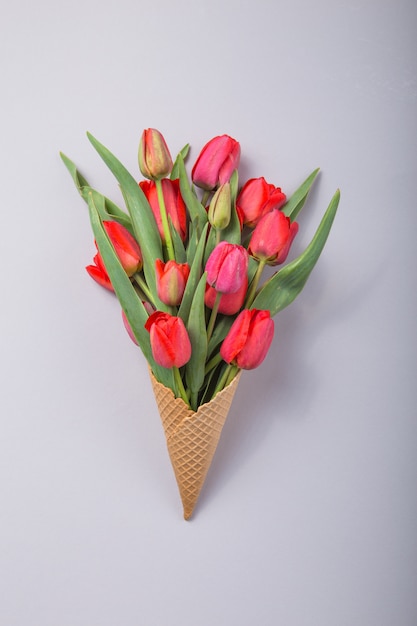 Belles tulipes rouges dans un cône de gaufre de crème glacée un fond de béton. Idée conceptuelle d'un cadeau de fleur. Humeur printanière