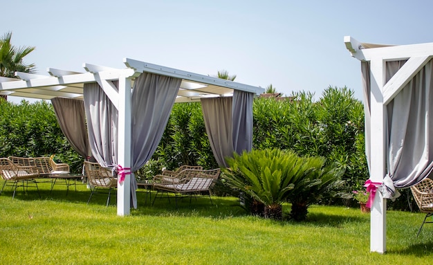 Belvédère en toile blanche avec mobilier de jardin en plastique dans une pelouse verte d'été