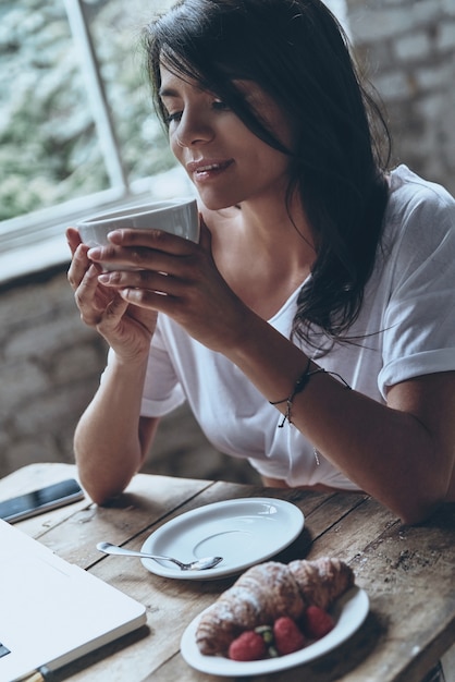 Bénéficiant d'un café chaud. Jolie jeune femme gardant les yeux fermés et souriant