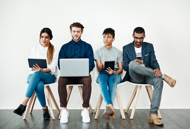 Bénéficiant de notifications instantanées et d'applications sans fin Photo d'un groupe de jeunes utilisant la technologie sans fil assis dans une rangée