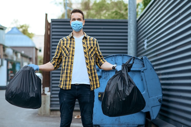 Le bénévole en masque tient des sacs poubelles en plastique à l'extérieur, faisant du bénévolat. Les gens nettoient les rues de la ville, la restauration écologique, la collecte et le recyclage des ordures, les soins écologiques, le nettoyage de l'environnement