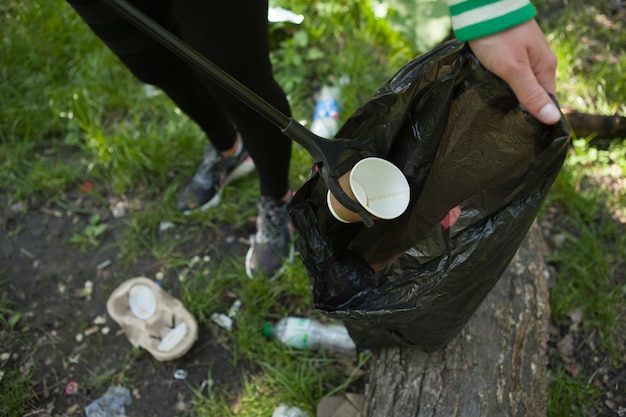 Photo bénévole méconnaissable mettant une tasse de café dans un sac poubelle, nettoyant dans la forêt
