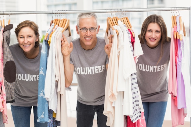 Bénévoles souriants debout entre les vêtements pendus