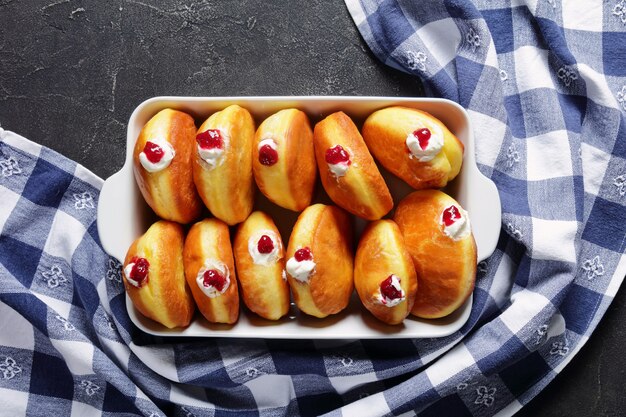 Berliner, beignets allemands faits maison avec confiture de framboises et garnitures à la crème dans un plat allant au four sur une table en béton, mise à plat, espace libre