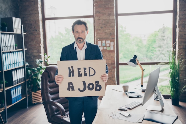 Photo besoin d'un travail. photo de profil d'un désespoir de mauvaise humeur licencié un employé de bureau homme mûr tenant une affiche à la recherche d'un nouvel emploi le dernier jour ouvrable lieu de travail congédié de mauvaise humeur bureau moderne à l'intérieur