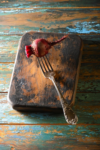 Betterave sur fourchette antique sur planche de cuisine brûlée sur table en bois teint rugueux
