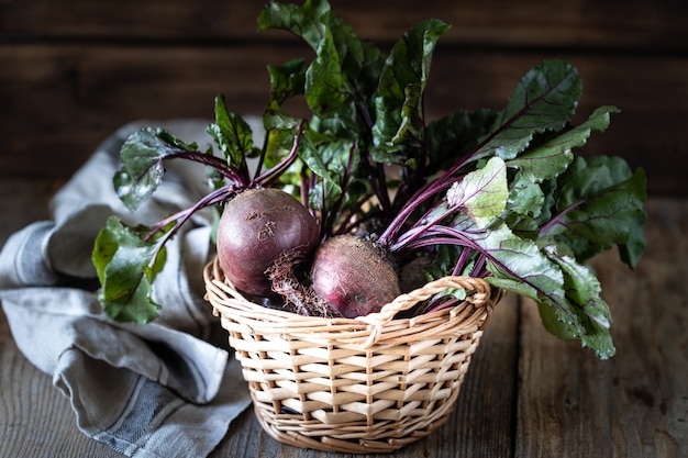 Betteraves rouges biologiques fraîches avec des feuilles dans un panier en osier sur une table en bois. Légumes biologiques naturels. Récolte d'automne. Rustique