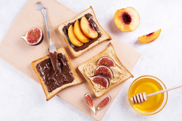 Beurre de cacahuète, chocolat à tartiner avec des fruits sur du pain grillé sur une planche à découper sur fond blanc, petit-déjeuner sucré sain, gros plan.