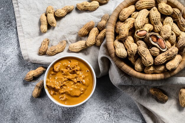 Beurre de cacahuètes dans un bol, cacahuètes crues, plats végétariens sains, vue de dessus.