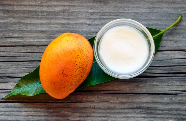 Beurre corporel à la mangue dans un bol en verre et mangue biologique mûre fraîche sur du vieux bois