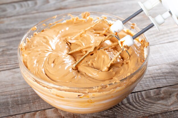 Beurre et lait concentré bouilli dans un bol en verre avec un mélangeur. Faire de la crème à gâteau