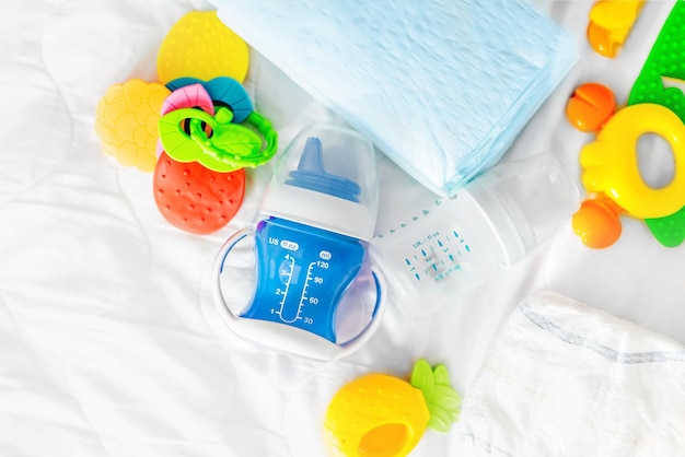 Biberon bleu d'eau couches bébé jetables jouets sur un lit blanc nourrissant des aliments complémentaires fo