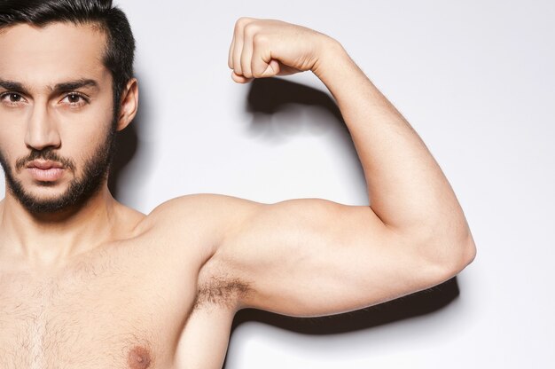 Biceps parfait. Gros plan d'un homme musclé montrant son biceps parfait en se tenant debout sur fond gris