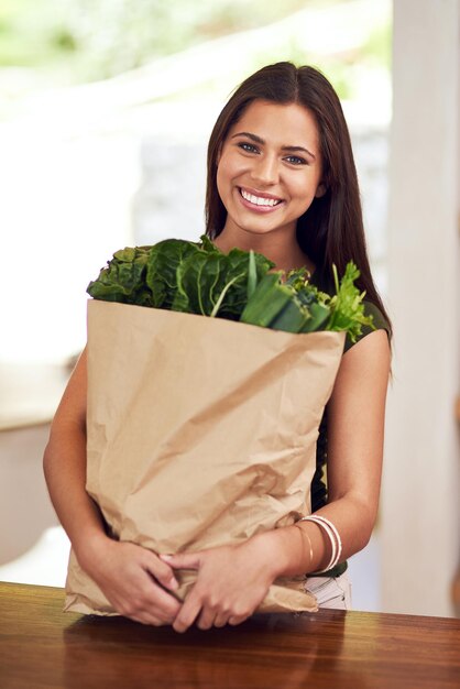 Bien manger et se sentir bien Portrait d'une jeune femme heureuse tenant un sac d'épicerie dans sa cuisine