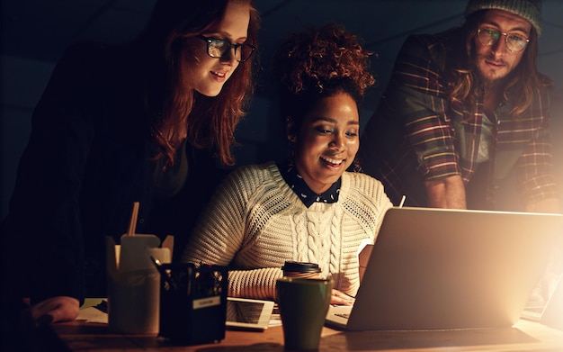 Bien réussir ensemble Photo d'une équipe commerciale utilisant un ordinateur portable ensemble pendant un quart de nuit au travail