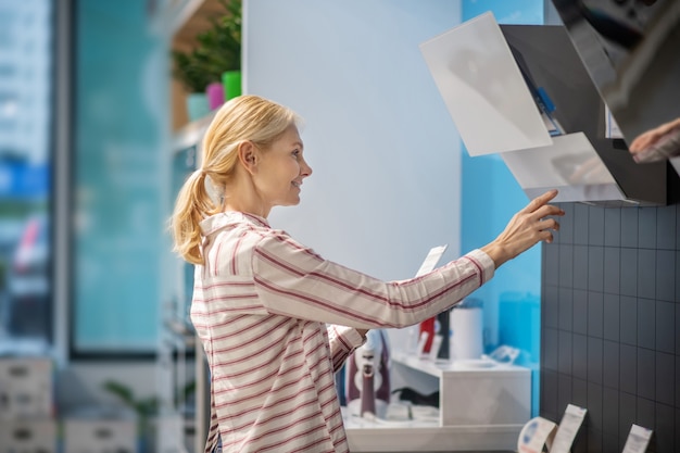 Biens de consommation. Cliente blonde choisissant des produits dans une salle d'exposition et à la recherche de participation