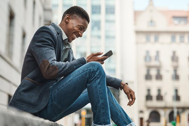 Photo bienvenue sur avenue success photo d'un jeune homme d'affaires assis sur le trottoir et utilisant un smartphone dans un contexte urbain