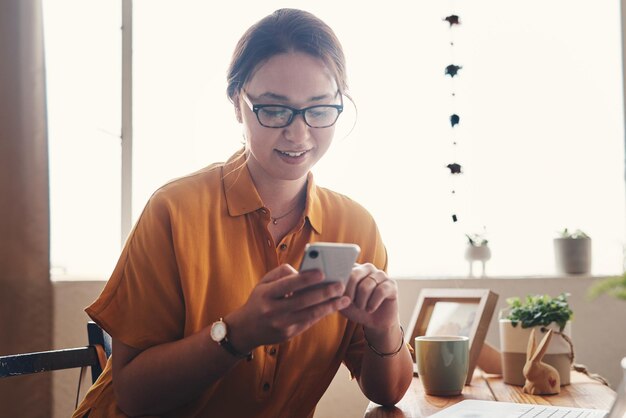 Bienvenue à l'ère numérique Photo recadrée d'une jeune femme d'affaires séduisante assise seule dans son bureau à domicile et envoyant des SMS sur son téléphone portable