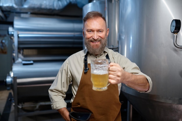 Photo bière artisanale fraîchement préparée en gros plan de verre. ouvrier de brasserie tenant une tasse avec de la bière fraîche. mise au point sélective. notion de brasserie