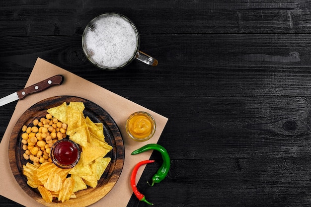 Bière blonde et collations sur table en bois noir chips de noix vue de dessus avec fond