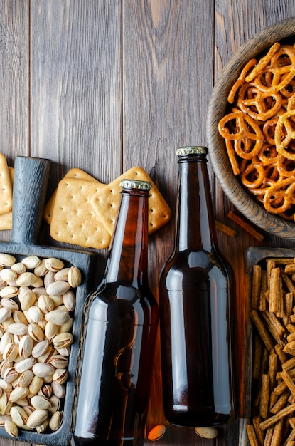 Bière en bouteilles en verre et collations salées pour bière dans des plats en bois. Style rustique. Fond en bois marron.