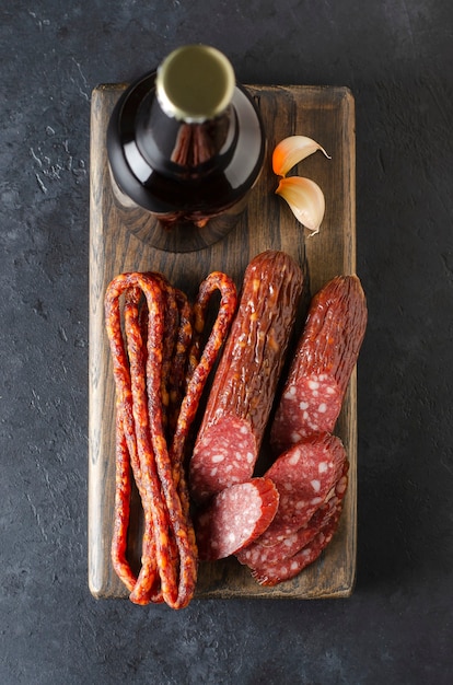 Bière en bouteilles de verre et saucisse. Fond de béton foncé.