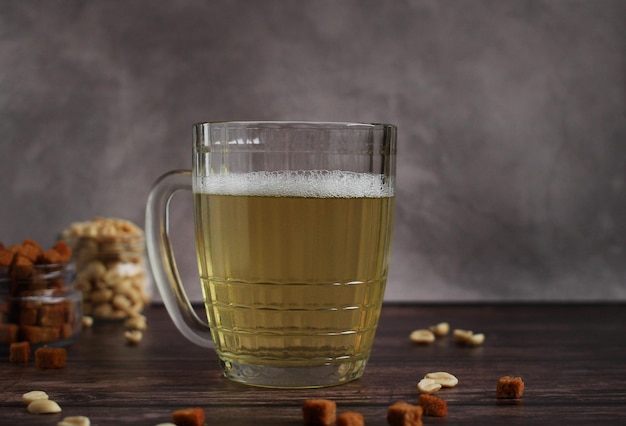 Bière légère dans une tasse en verre avec des craquelins et des cacahuètes sur fond sombre