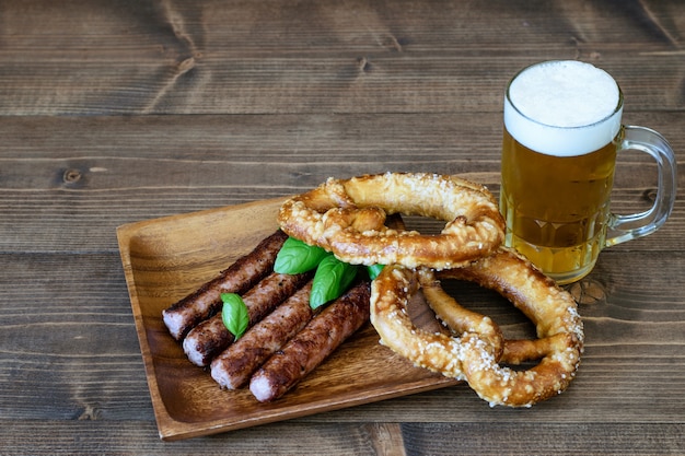 Bière légère servie avec des saucisses frites et des bretzels sur bois