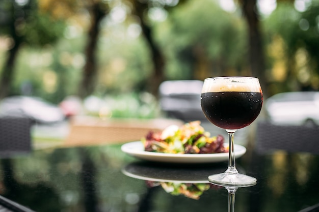 Bière à la pression sombre dans un verre avec un plat sur la table en verre en plein air