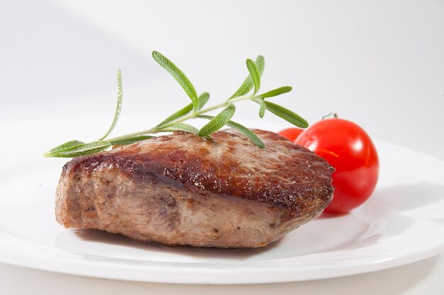 Bifteck appétissant bien fait d'un plat blanc avec des tomates et du romarin